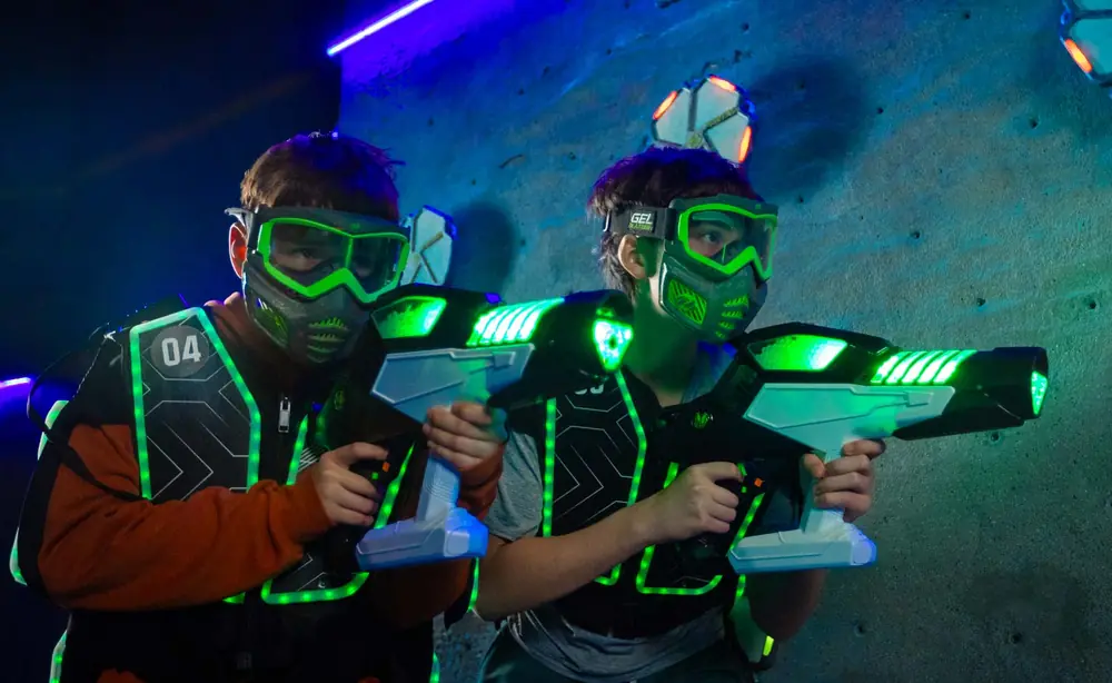 Two players in glowing vests holding laser tag blasters